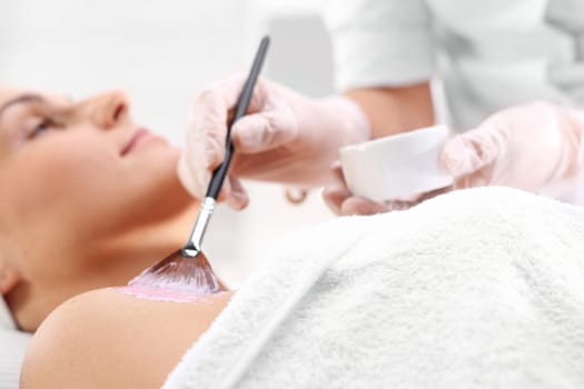 a woman in a beauty salon,a beautician applies a cleavage mask with a brush\n