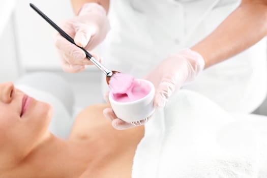 a woman in a beauty salon,a beautician applies a cleavage mask with a brush\n