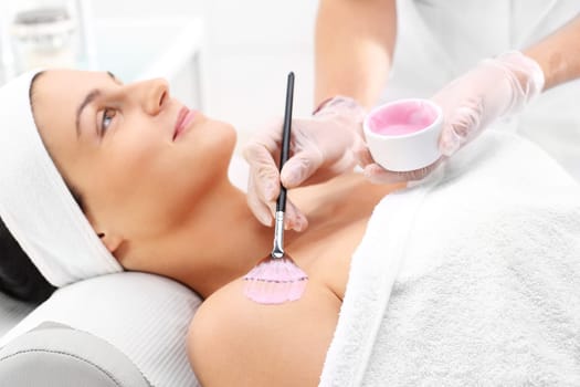 a woman in a beauty salon,a beautician applies a cleavage mask with a brush\n