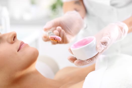 a woman in a beauty salon,a beautician applies a cleavage mask with a brush\n