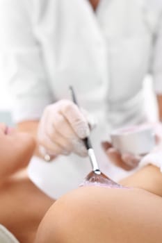 a woman in a beauty salon,a beautician applies a cleavage mask with a brush\n