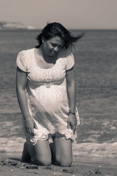 Portrait of a beautiful happy pregnant woman on the beach, kneeling and looking down. Focus on the belly.