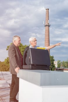 Two senior businessmen with briefcase discussing business outdoors on the roof of a building.
