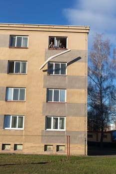 Two seniors throwing rolled carpet out of a window from the top floor of a building.
