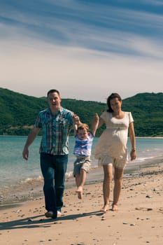 Happy pregnant couple and their son enjoying sunny day, jumping and walking on the coast in Spain.