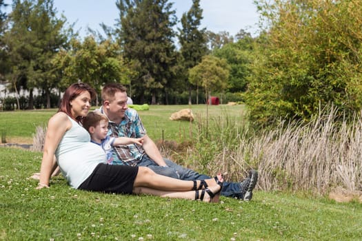 Young happy pregnant family relaxing in the park and enjoying summer day outdoors.