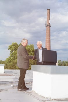 Two senior businessmen with briefcase handshaking and making a business deal outdoors on the roof of a building.