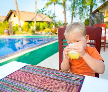 Child drinking juice near a swimming pool