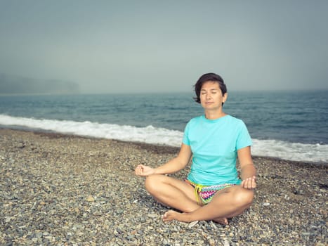 Woman meditating at seaside. Foggy weather