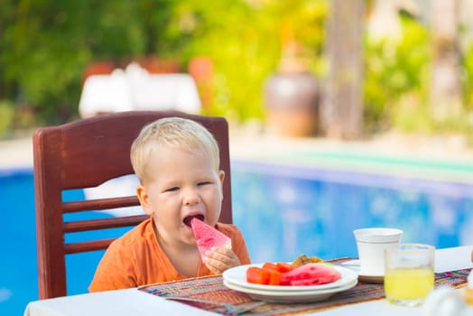 Child has a breakfast near a swimming pool
