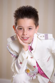 Young boy resting his head on his hand and looking at camera celebrating his First Holy Communion