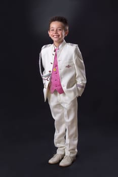 Young boy celebrating his First Holy Communion looking at camera and standing on a black background.