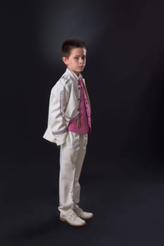 Young boy in his First Holy Communion looking at camera and standing with a serious expression on a black background.