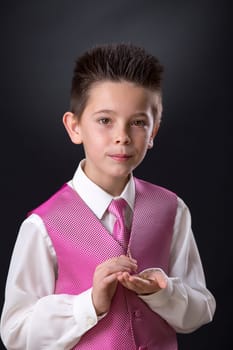 Young boy celebrating his First Holy Communion holding his medals and looking at camera on a black background.