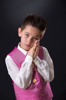 Young boy celebrating his First Holy Communion holding his rosary and looking at camera on a black background.