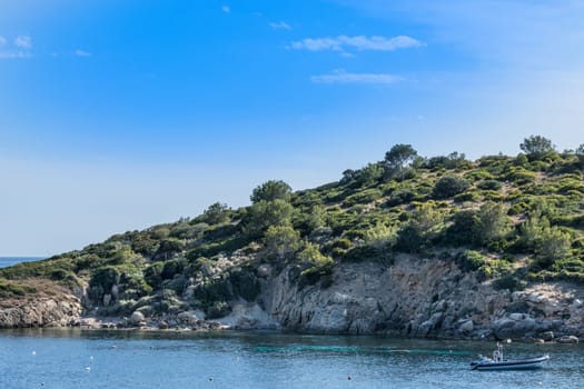 Rocks in the Mediterranean with small inflatable boat at anchor..