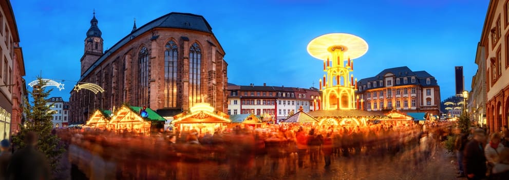 Christmas market in Heidelberg,Germany,a panorama shot at dusk showing illuminated kiosks,historic architecture and blurred people
