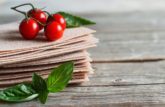 Raw lasagna sheets, basil and cherry tomatoes on a wooden table close up