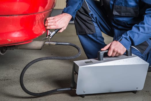 A diagnostic sensor is applied to the ehaust of a red car, measuring the composition and substances in the exhaust fumes in a garage, given the crisis Volkswagen is facing due to their faked