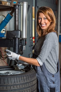 Young Female car mechanic changing car tyre in auto repair shop with a machine and a big wrench