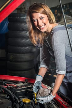 Young smiling female car mechanic in auto repair service, red automobile with tire in background