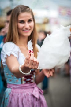 Beautiful young smiling woman wearing a traditional Dirndl dress with cotton candy floss at the Oktoberfest.