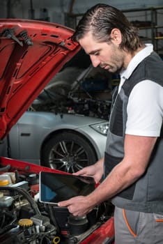 Mechanic using a tablet pc at the repair garage, red automobile