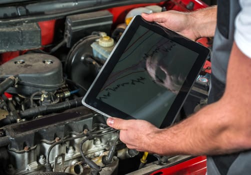Mechanic using a tablet pc at the repair garage, red automobile