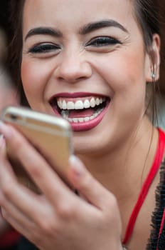 Girl in traditional Dirndl dress, Asian and German multi-racial, drinking beer and having fun while using her mobile phone at Oktoberfest