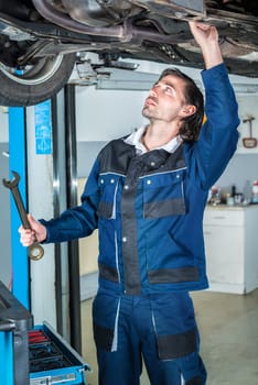 Portrait of a young male mechanic repairing a lifted car with a  big wrench