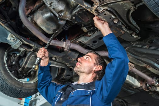Portrait of a young male mechanic checking the condition of a lifted car