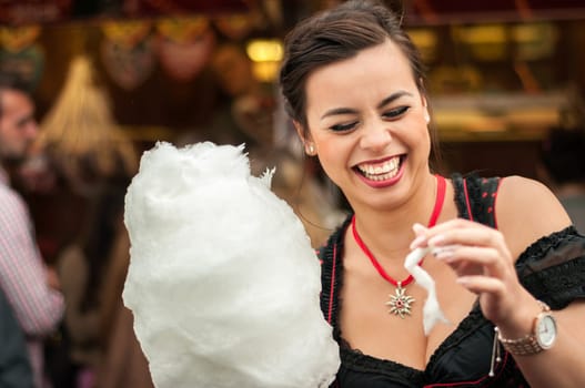 Beautiful young smiling woman wearing a traditional Dirndl dress with cotton candy floss at the Oktoberfest.