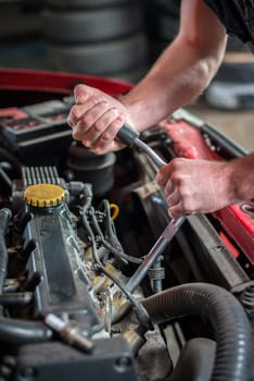 Hands of a car mechanic in auto repair service, starting ignition plug, red automobile