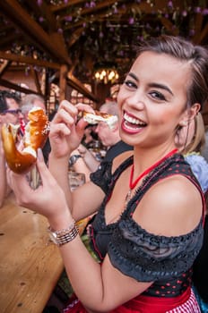 Attractive young woman in traditional Dirndl ot tracht eating Oktoberfest Pretzel, multi-racial Asian, from the Philippines and Caucasian mix