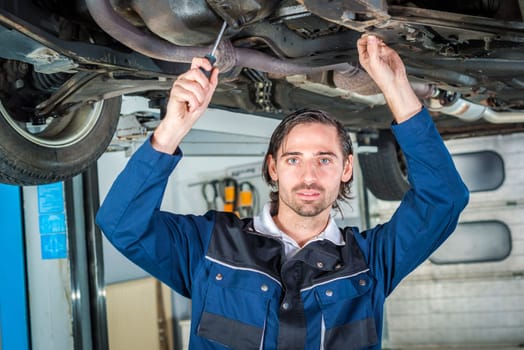 Portrait of a mechanic checking the condition a lifted red car