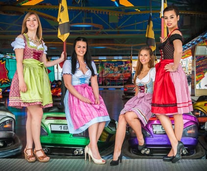 Joyful and attractive women at Oktoberfest with traditional dirndl dresses, autoscooter in the background. Mixed nationalities, German, Asian, Slavic
