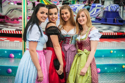 Joyful young and attractive women at German funfair Oktoberfest with traditional dirndl dresses and joyride in the background. Mixed nationalities.