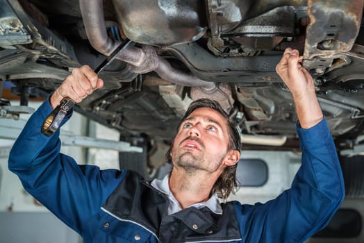 Portrait of a young male mechanic repairing a car, a lifted car