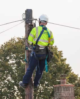 FAKENHAM, NORFOLK / UK - 10th OCTOBER 2016: Openreach BT engineer fixing cables up a pole. UK internet and telephone infrastructure provider at work providing internet and telephone services to rural locations