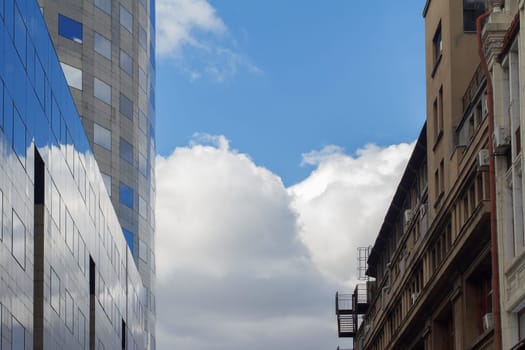 Side by side photo of classical building in front of modern glass office building with blue sky in between