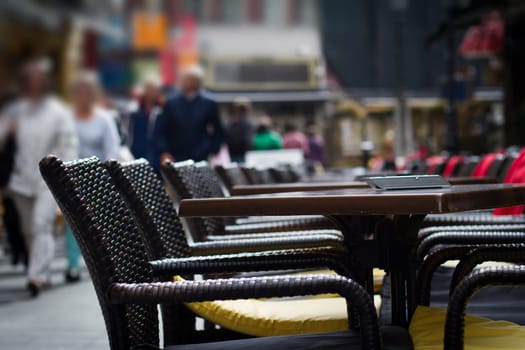 Tables and chairs on a terrace in front of restaurant with people walking by in the background