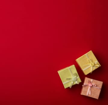 Top view of three small cardboard rectangular gift boxes on red paper background with copy space