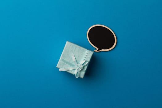 top view of small gift box on blue background with wooden black chalk board speech bubble for text