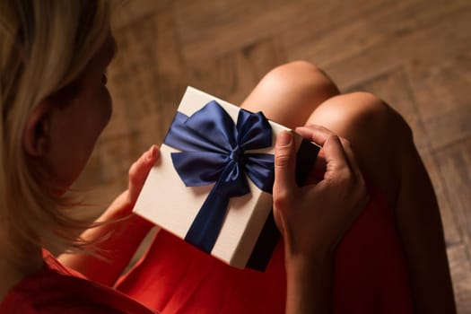 Top view woman opening a present with blue ribbon with three gift boxes inside on her knees