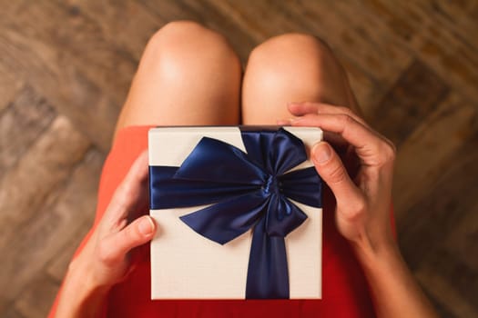 Top view woman with red dress holding a gift box with blue ribbon on her knees