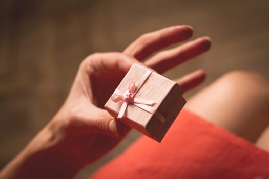 Woman with pink dress opening a small gift box above her knees