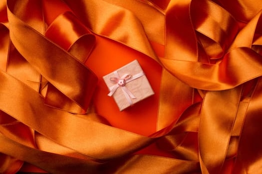 Top view of centered pink small gift box with orange ribbon background around it
