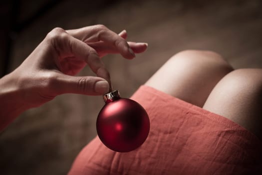 Woman with red dress holding a red Christmas globe with her fingers