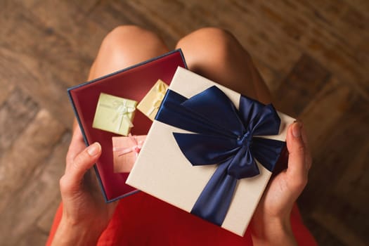 Top view woman opening a present with blue ribbon with three gift boxes inside on her knees