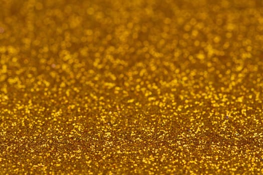 Horizontal glittery gold colored background texture with blurry depth of field